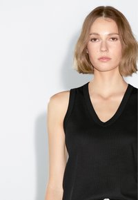 Top nero senza maniche con scollatura a V, realizzato in un tessuto liscio, caratterizzato da una vestibilità aderente e una superficie texture.