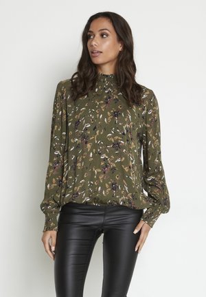 Blouse à motif floral vert avec un col haut et des manches longues, associée à un pantalon en cuir noir. Comprend un tissu doux et une coupe décontractée.