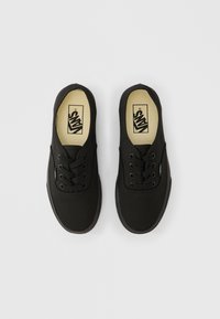 Baskets en toile noire avec semelles en caoutchouc, bout rond, design à lacets et logo sur la languette. Texture simple et lisse sans motifs.