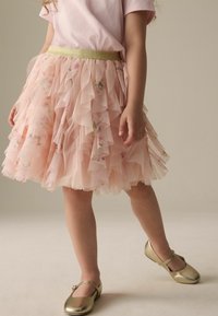 Rosa Tüllrock mit geschichteten Rüschen und floralen Akzenten, kombiniert mit goldenen Ballerinas. Der goldene Taillenbund verleiht dem Design eine besondere Note.