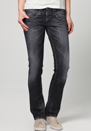 Dunkelblaue Jeans mit slim Fit, die leichte Waschung, ein Five-Pocket-Design und sichtbare Nähte aufweisen. Kombiniert mit beigen Sneakers.