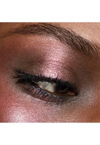 Gros plan sur un œil fermé avec un fard à paupières rose et bronze scintillant, de longs cils noirs et une texture de peau lisse et foncée autour de l'œil.