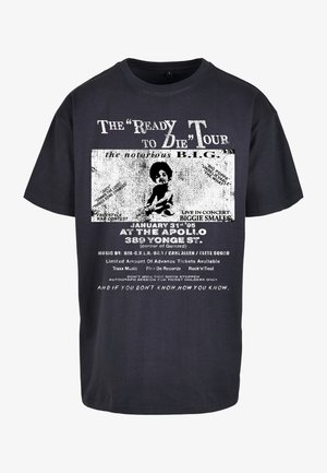 Black cotton T-shirt featuring a vintage design, white text, and graphic illustration of a seated child. Text emphasizes a concert event.