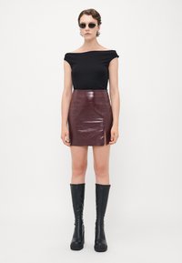 Kvinne i svart av-shoulder topp, glitrende mørk burgunder mini skjørt med en liten frontslitt, knelengde svarte plattform støvler og solbriller.