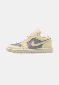Beige Nike sportcipők, amelyek oldalain világoskék és levendula színű átmenetet mutatnak, klasszikus alacsony felső kialakítással és fűzős elemmel.