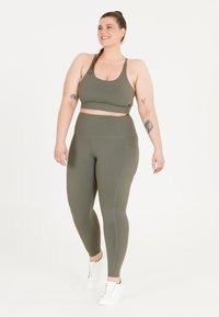 Oliivinvihreä aktiivivaatetussetti, johon kuuluu spagettiolkaimilla varustettu crop-top ja korkeat leggingsit, joissa on saumatonta muotoilua ja taskuyksityiskohta.
