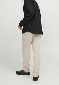Maglietta nera a maniche lunghe, vestibilità ampia, abbinata a pantaloni beige chiaro e scarpe slip-on nere con suola spessa.
