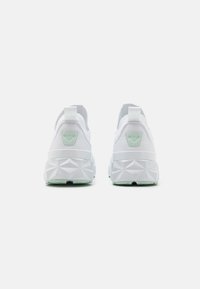 White sneakers with geometric-patterned soles and light green logo patches on the heel, shown from the back on a plain background.