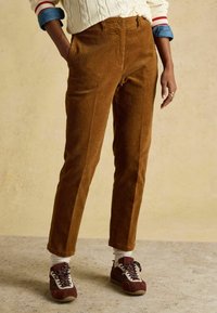 Brūnas kordurojas bikses ar taisnu griezumu, ar priekšējām kabatām un pogas aizdari, kombinētas ar sarkani baltām kedām un baltām zeķēm.