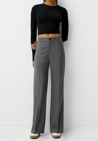 Grijs gestreepte wijde broek met een hoge taille en knoopsluiting, gecombineerd met een fitted zwart longsleeve-top. Casual schoenen zichtbaar.