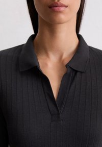 Schwarzes Poloshirt mit vertikaler Ripp-Textur, ausgestattet mit einem klassischen Kragen und einem Ausschnitt-Detail am Hals. Weicher Stoff.