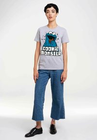 Gray cotton T-shirt featuring a large blue Cookie Monster graphic with a cookie, paired with light blue wide-leg jeans and black shoes.