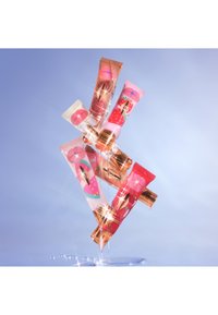 Six colorful cosmetic tubes arranged in a dynamic formation. They feature fruit illustrations and shiny gold accents on a gradient background.