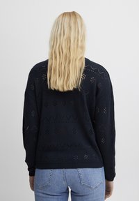Tumesinine kudum-sviiter avatud töötlusega mustriga, millel on geomeetrilised kujundid ja mansetid, millel on soonikkoes detailid, kombineeritud helesinine denim.