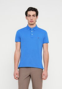 Μπλε βαμβακερό πόλο πουκάμισο με κλασικό γιακά, τρία κουμπιά και κοντά μανίκια. Διαθέτει μικρό λογότυπο στην αριστερή πλευρά.