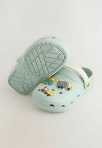 Svetlozelené nepremokavé šľapky s ventilačnými otvormi, zdobené farebnými dekoráciami s motívmi vozidiel a bielym opaskom na päte pre podporu.