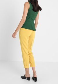 Zelený peplum top z texturované látky, zkombinovaný se střiženými žlutými kalhotami. Kalhoty jsou po kotníky s ohrnutými manžetami. Černé muly doplňují celý outfit.