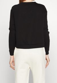 Sudadera negra corta con cuello redondo, mangas largas y puños acanalados. Tela suave con una textura lisa y un diseño mínimo.