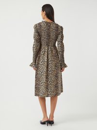 Leopardmönstrad klänning med långa puffärmar, smockad byst och en flödande kjol. Tyget har en texturerad yta med svarta och beige mönster.