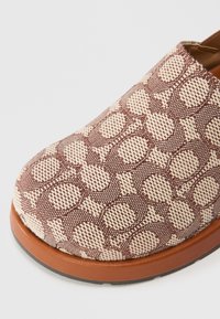 Instap-schoen van bruin geweven stof met een beige cirkelpatroon. Rubberen zool met een lichte verhoging, een gladde textuur en subtiele stikseldetails.
