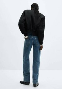 Schwarze, verkürzte Bomberjacke, blaue Jeans und schwarze, Absatzankelstiefel. Glatter Stoff, lockere Passform und ausgefallene Taschenverarbeitung.