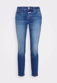 Blå slimfit-jeans med fem fickor och urtvättning på framsidan och benen mot en enfärgad vit bakgrund.