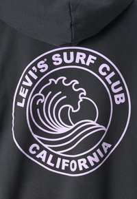 Sudadera gris con un gráfico circular que presenta una ola lavanda y el texto "LEVI'S SURF CLUB CALIFORNIA" en una fuente en negrita. Textura suave.
