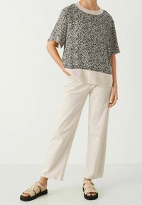 Zwart-witte spikkelige top met korte mouwen en een effen lichtbeige zoom, gecombineerd met crèmekleurige brede broek en tan sandalen met zwarte zolen.