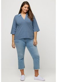 Blå og marineblå stribet v-hals top med trekvartærmer, parret med lyse, cropped jeans og hvide sneakers. Afslappet outfit.