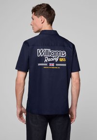 Granatowa koszula na krótki rękaw z logo "Williams Racing" w białym i żółtym na plecach, z motywem w kratę i detalem flagi brytyjskiej.