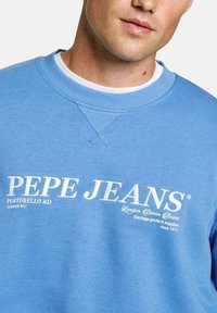 Svijetloplavi dukserica s okruglim izrezom, rebrastim manžetama i bijelim grafičkim tekstom koji glasi "PEPE JEANS" uz detalje logotipa.