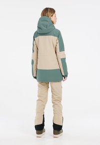 Damen Außenjacke in zweifarbiger Optik in Beige und Grün, ausgestattet mit Kapuze, elastischen Bündchen und einem lässigen Schnitt, kombiniert mit Cargo-Hosen in Beige.