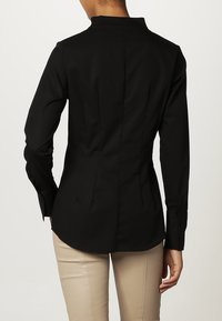 Camicia nera aderente con colletto alla mandarino, maniche lunghe e polsini con bottoni. Presenta cuciture verticali e un design a vita stretta.