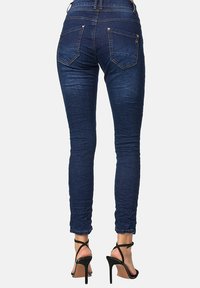 Jeans ajustados de color azul oscuro con una textura suave, que presentan bolsillos traseros y un diseño ajustado. Combinados con tacones altos negros con tiras.