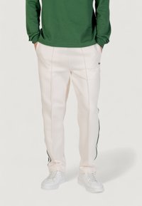 Cremefarbene, lässig geschnittene Hose mit kontrastierenden dunkelgrünen Seitenstreifen und weißen Nähten, kombiniert mit einem grünen Langarmshirt und weißen Sneakers.