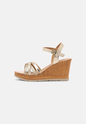 Kilesandal med metalliske gyldne stropper, ankelspænde og kilehæl med vævet tekstur, vist på hvid baggrund.