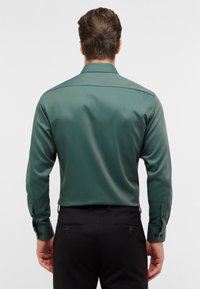 Groen overhemd met lange mouwen en een gladde textuur, met een puntige kraag en knoopmanchetten. Gekozen in combinatie met zwarte broek.