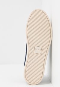 Baskets bleu marine avec une semelle en caoutchouc texturée, ornée de lignes horizontales en relief et d'un logo carré CLAE. Design simple avec des accents minimaux.