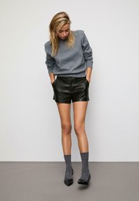 Maglione grigio a maglia, pantaloni corti in pelle nera, calze grigie e scarpe a punta nera. Texture lisce e design aderente.