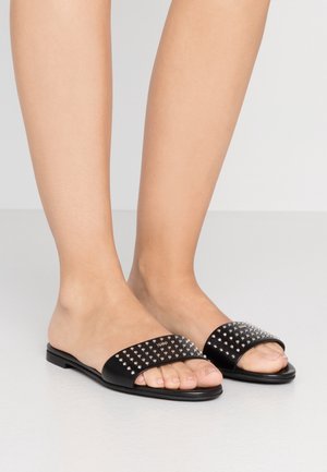 Černé kožené pantofle s plochou podrážkou a širokými pásky ozdobenými stříbrnými nýty, které mají hladkou texturu a minimalistický design.