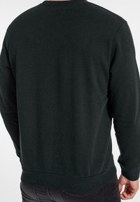 Mörkgrön långärmad sweatshirt med rund halsringning, med en slät textur och ribbade muddar. Bakifrån syns inga synliga logotyper eller mönster.