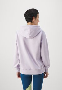 Felpa viola chiaro con una texture morbida, cappuccio regolabile e polsini a costine. Abbinata a leggings blu aderenti con un accento verde.