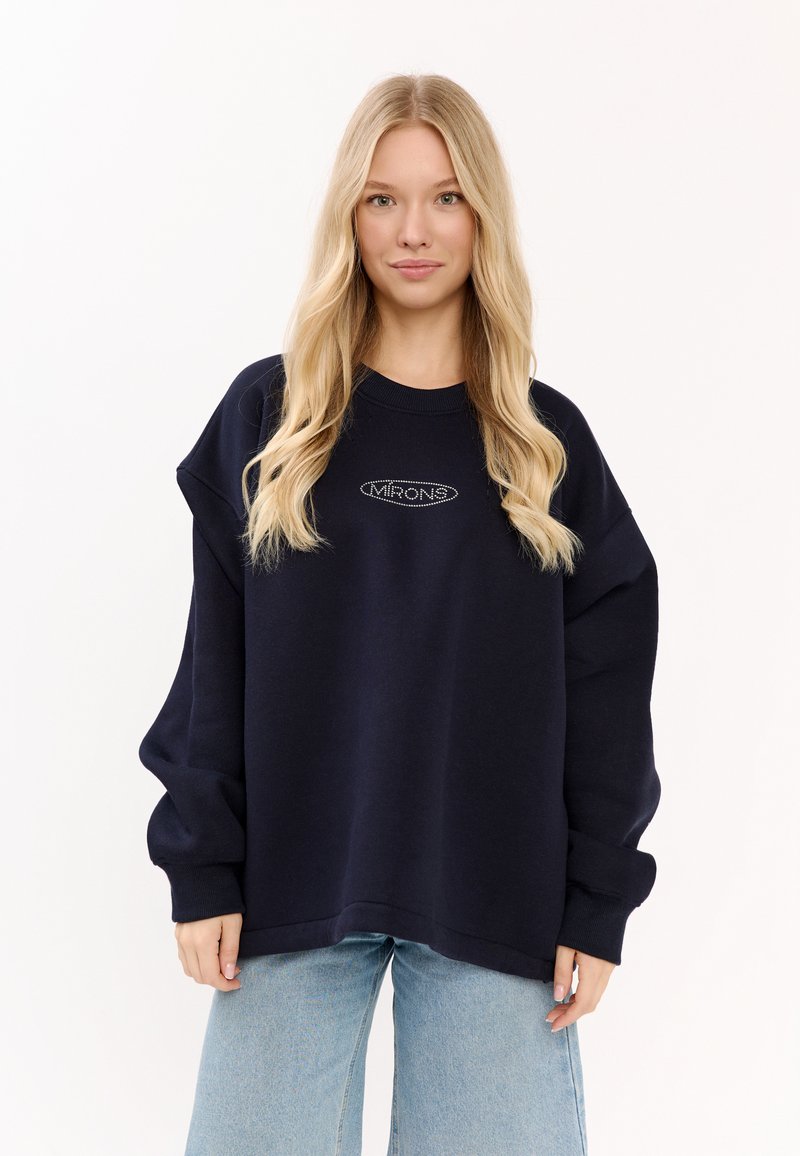 Granatowy, oversize'owy sweatshirt z prążkowanym dekoltem, opuszczonymi ramionami oraz subtelnie wyhaftowanym logiem "MIRONS". W połączeniu z jasnymi dżinsami.