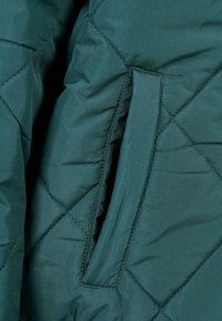 Wytłaczany zielony puchowy jacket z diamentowym szwem. Posiada boczną kieszeń. Gładka faktura o matowym wykończeniu.