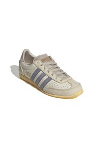 Beżowe sneakersy z szarymi akcentami, z trzema fioletowymi paskami, perforowanymi szczegółami, okrągłym noskiem, teksturowaną gumową podeszwą oraz sznurowanym zamknięciem.