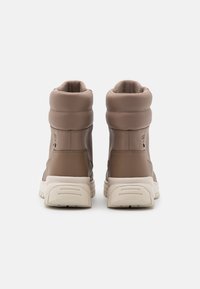 Brązowe, wysokie skórzane buty z wyściełanym kołnierzem, teksturowaną powierzchnią i solidną białą gumową podeszwą. Charakteryzują się smukłym designem i minimalistycznymi detalami.