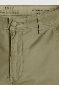 Pantalon chino khaki Levi's XX avec fermeture par bouton, passants de ceinture et étiquette « Authentic Straight » indiquant la taille W32.