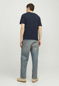Marine crewneck t-shirt, relaxed fit, gecombineerd met lichtblauwe denim jeans. Casual schoeisel in beige, met een subtiele textuur en detail.