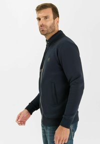 Felpa con zip di colore blu navy, colletto alto, tasche frontali, polsini a costine e un delicato dettaglio del logo sul petto. Composizione in morbido cotone e poliestere.