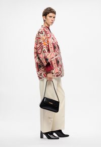 Mintás dzseki rózsaszín, piros és fekete geometrikus mintákkal, krémszínű nadrággal és fekete kézitáskával párosítva. Fényes fekete magassarkú csizmák.